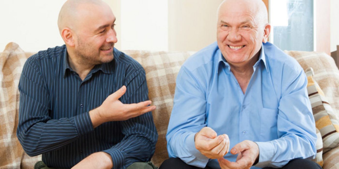 Zwei Männer, glatzköpfig, Freizeithemden, ca. um die 60, auf Couch beim fröhlichen Unterhalten