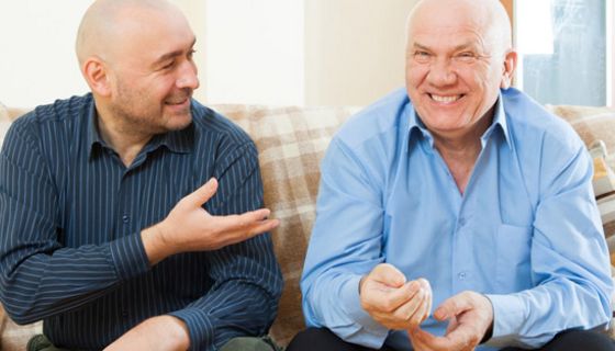 Zwei Männer, glatzköpfig, Freizeithemden, ca. um die 60, auf Couch beim fröhlichen Unterhalten