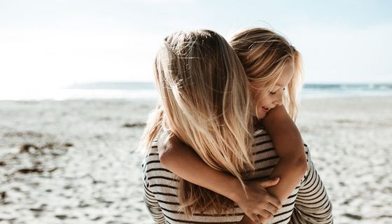 Mädchen, umarmt ihre Mutter am Strand.