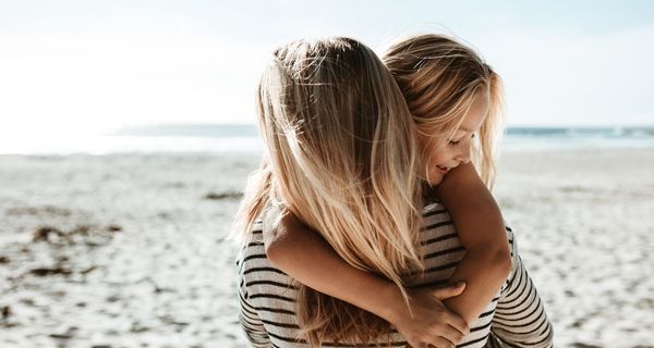 Mädchen, umarmt ihre Mutter am Strand.