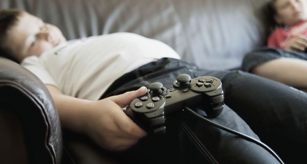 Übergewichtiger Junge mit Gaming-Controller auf der Couch.