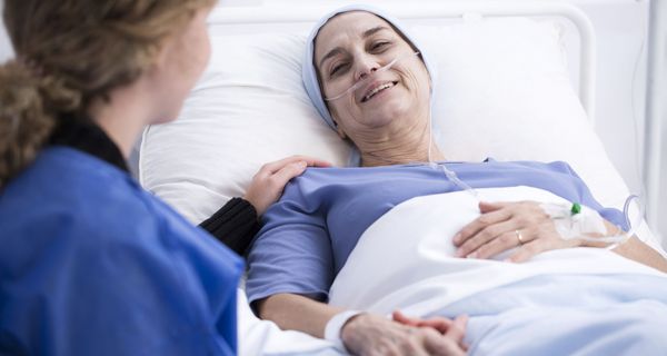 Pflegerin spricht mit Patientin, die im Krankenhausbett liegt.