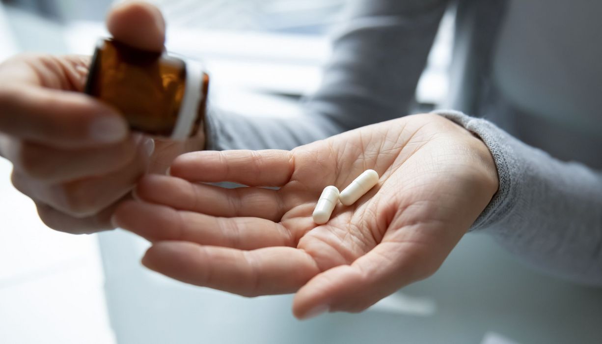Frau, schüttet Tabletten aus einer Glasflasche auf die Hand.