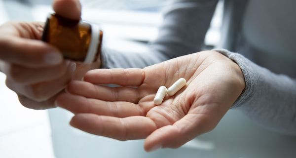 Frau, schüttet Tabletten aus einer Glasflasche auf die Hand.