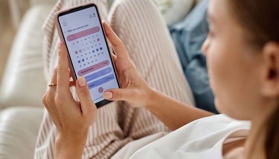 Frau, schaut auf ihr Smartphone mit Zyklusdaten.
