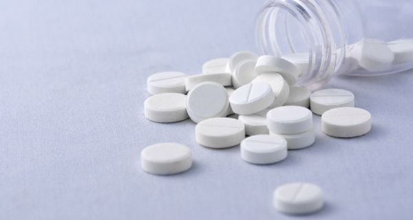 Arzneifläschchen aus Glas, davor ausgeschüttete weiße Tabletten