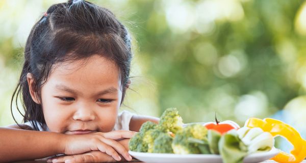 Kind, schaut kritisch einen Teller mit Gemüse an.