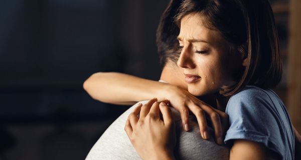 Frau, wird von einem Mann umarmt, ihr laufen Tränen die Wange herunter.