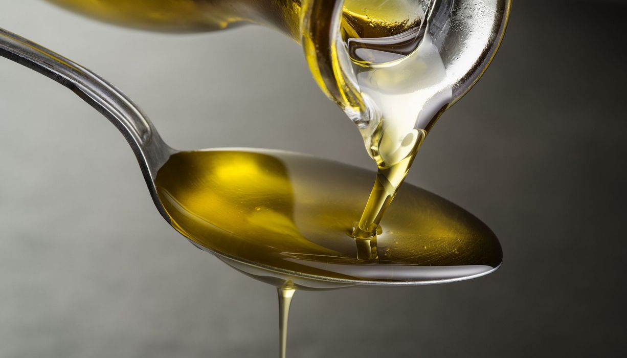 Olivenöl fließt aus Kanne auf einen Löffel.