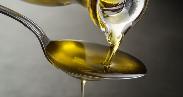 Olivenöl fließt aus Kanne auf einen Löffel.