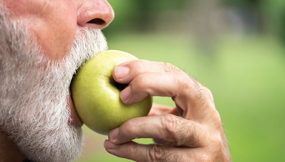 Älterer Mann, beißt in einen Apfel.