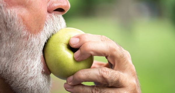 Älterer Mann, beißt in einen Apfel.