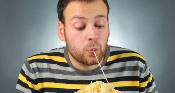 Junger Mann zieht mit den Lippen eine Spaghetti ein von einem großen Teller vor sich