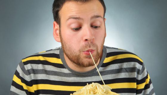 Junger Mann zieht mit den Lippen eine Spaghetti ein von einem großen Teller vor sich