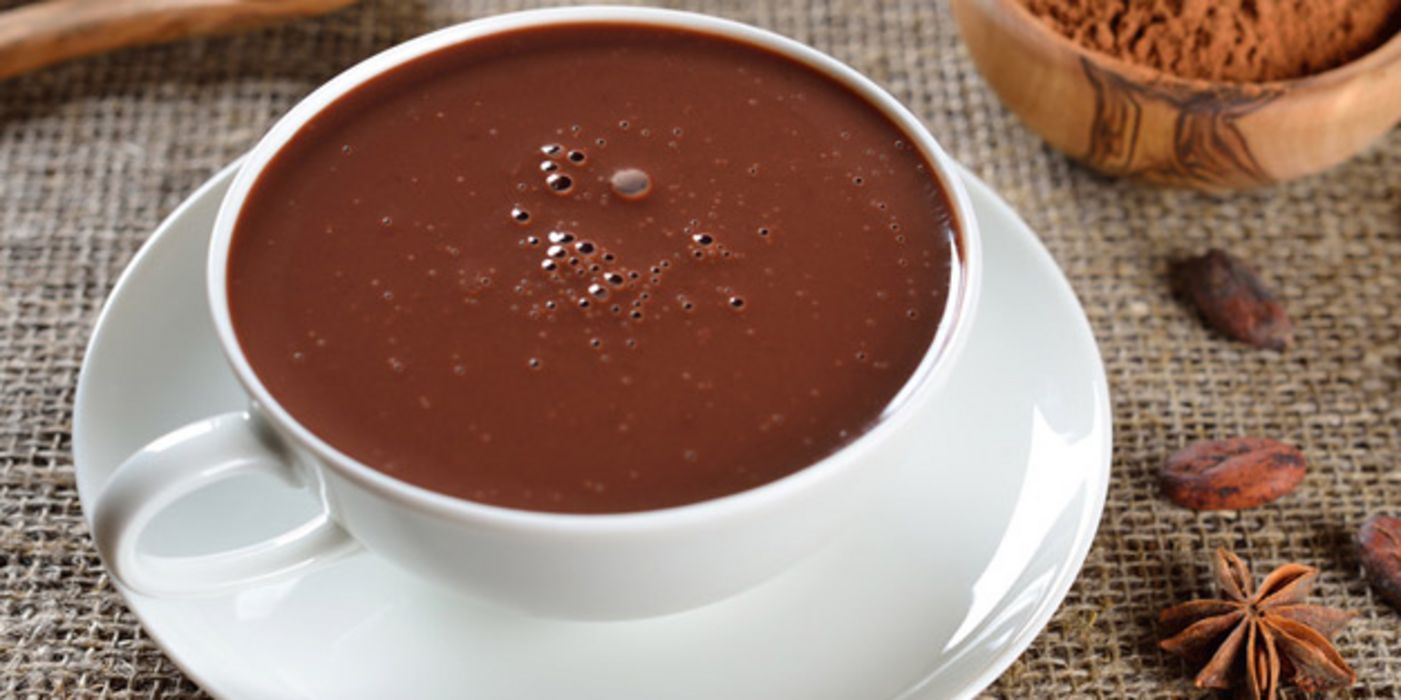 Tasse mit dunklem Kakao und Kakaobohnen daneben