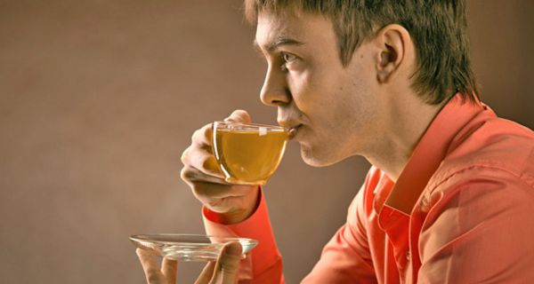 Profil junger Asiate führt eine Glasteetasse mit grünem Tee zum Mund