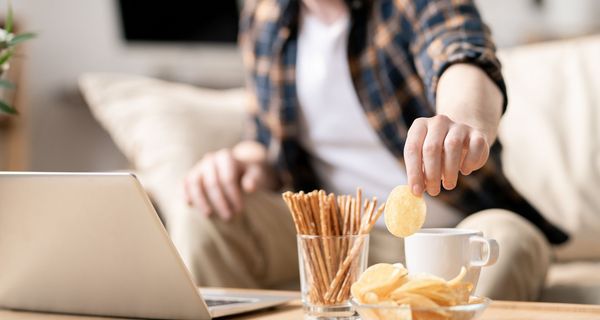 Mann, sitzt am Laptop und isst Chips.