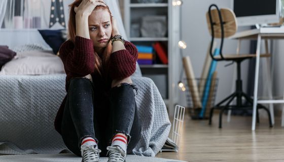 Junges Mädchen, sitzt in ihrem Zimmer auf dem Boden und sieht verzweifelt aus.