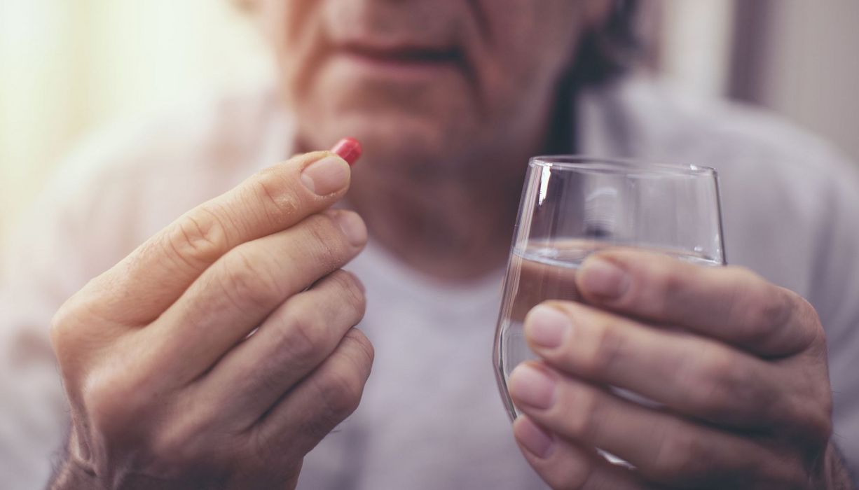 Ältere Mann, hält ein Glas Wasser und eine Tablette in der Hand.