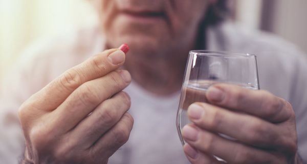 Ältere Mann, hält ein Glas Wasser und eine Tablette in der Hand.