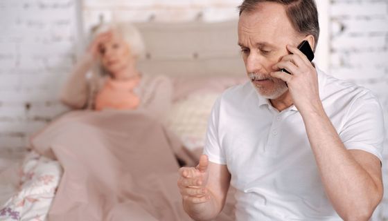 Mann telefoniert, im Hintergrund liegt eine Frau im Bett.