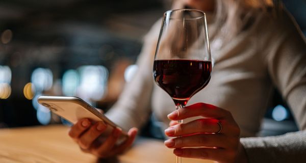 Frau mit Smartphone und einem Glas Rotwein in der Hand.