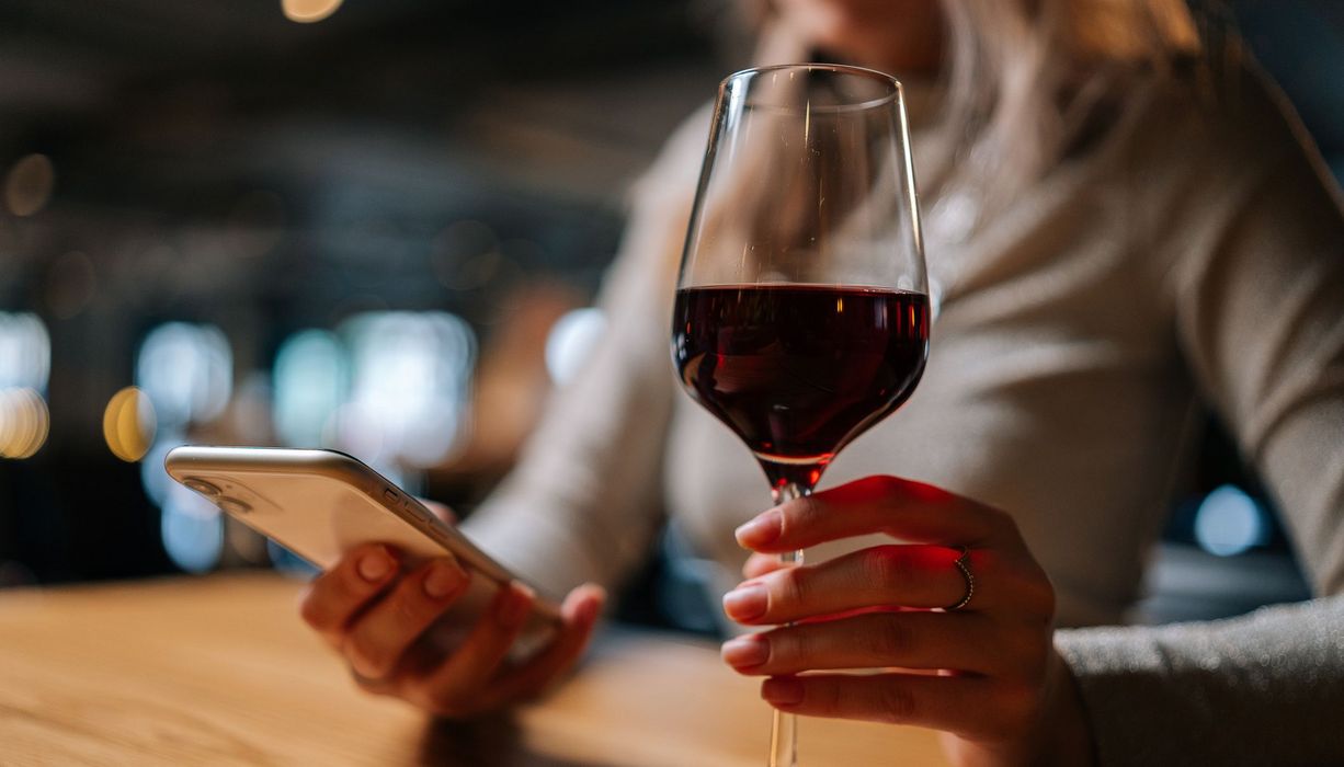 Frau mit Smartphone und einem Glas Rotwein in der Hand.