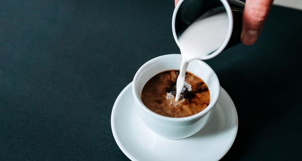 Frau, gießt Milch in eine Tasse Kaffee.