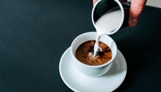 Frau, gießt Milch in eine Tasse Kaffee.