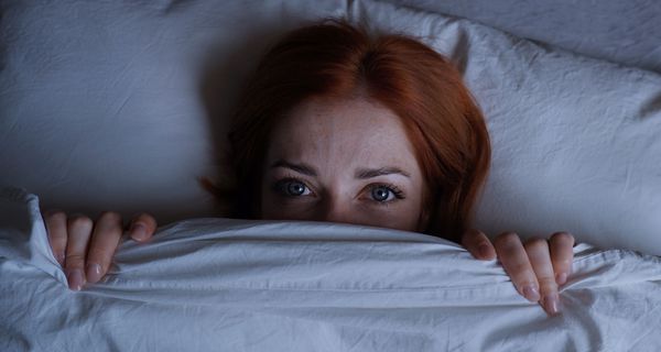 Junge Frau, liegt ängstlich im Bett.