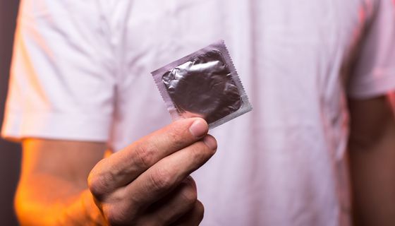 Mann, hält ein Kondom zum Schutz vor sexuell übertragbaren Erkrankungen wie Tripper in die Kamera.