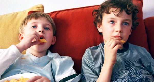 Zwei Kinder schauen TV und futtern Chips