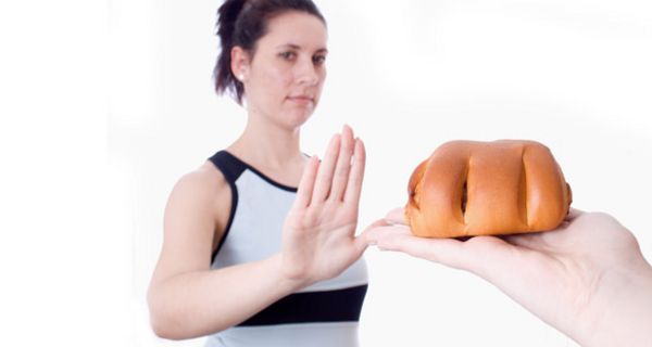 Junge Frau weist das ihr auf einer Hand angebotene Backwerk mit einer abweisenden Geste zurück