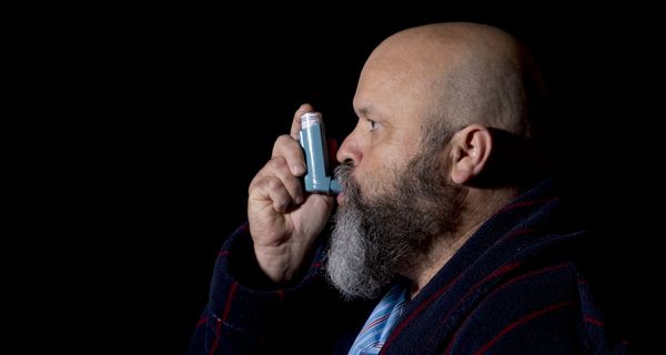 Bärtiger Mann inhaliert Asthmaspray.