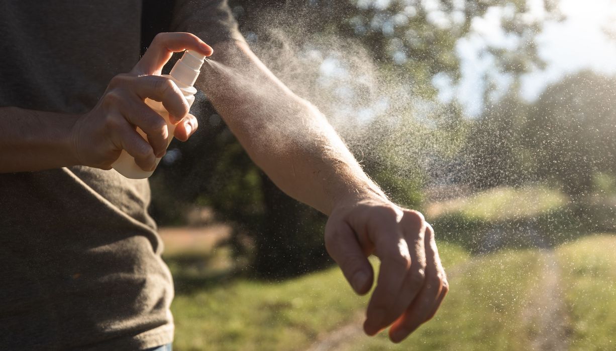 Mann, sprüht sich mit Mückenspray ein.