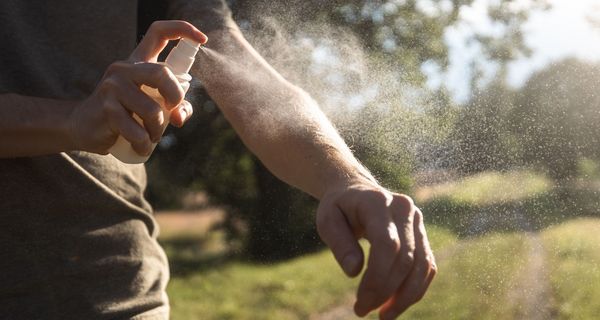 Mann, sprüht sich mit Mückenspray ein.