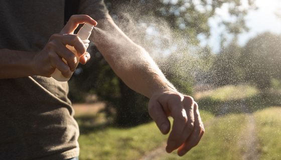 Mann, sprüht sich mit Mückenspray ein.