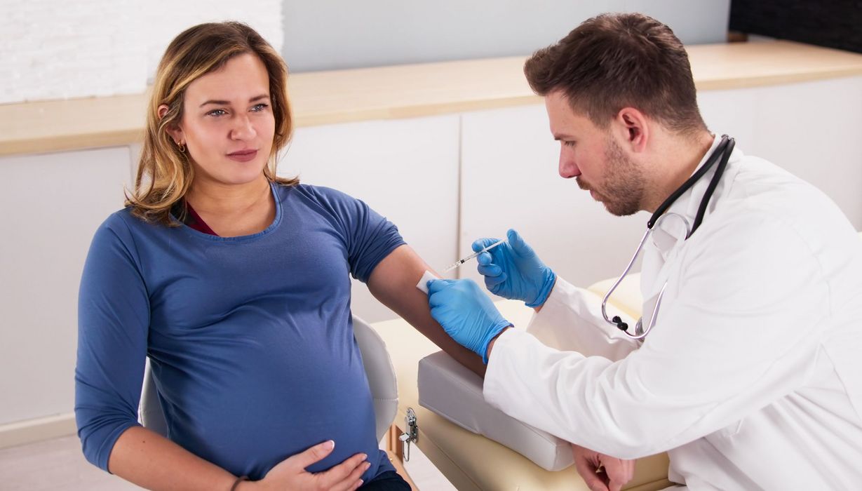 Ein Arzt impft eine Schwangere, die dabei sehr ruhig und gelassen wirkt..