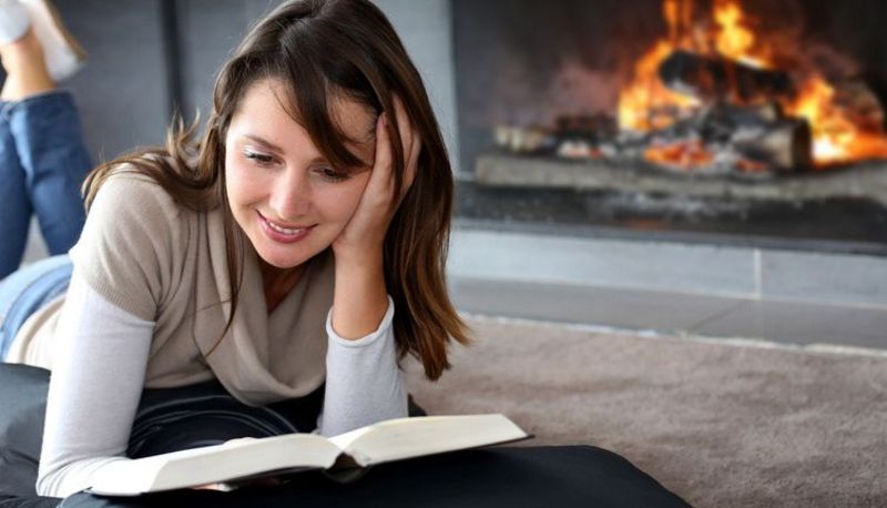Junge Frau liegt vor einem Kamin und liest ein Buch