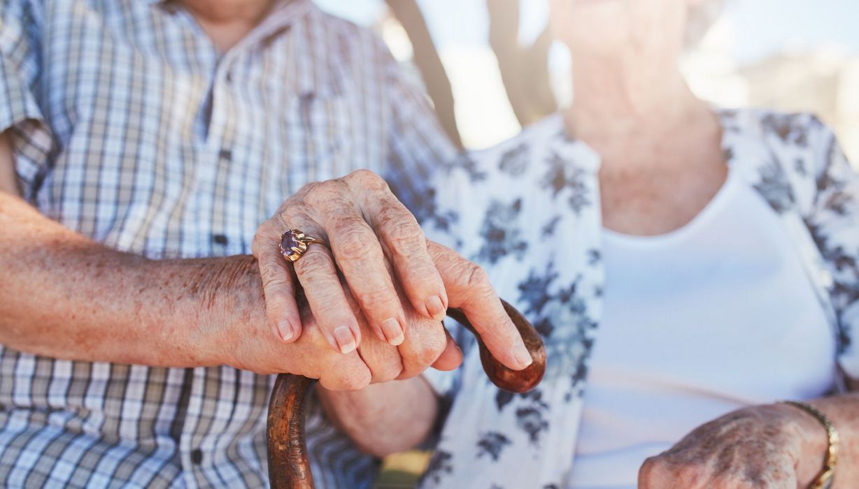 Älterer Mann und Frau, stützen sich auf Gehstock und halten sich an der Hand, Nahaufnahme.