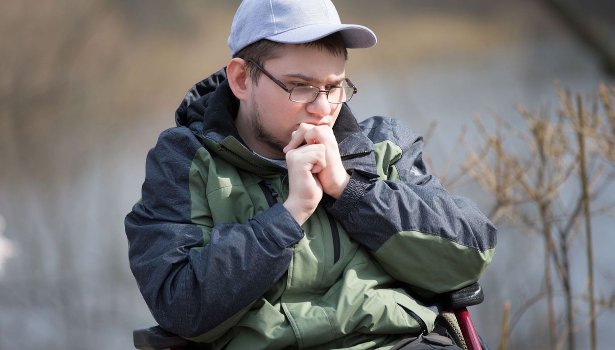 Ein junger Mann im Rollstuhl blickt traurig.