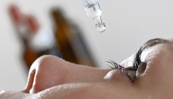 Frau mit geschminktem Auge tropft sich Augentropfen ins Auge