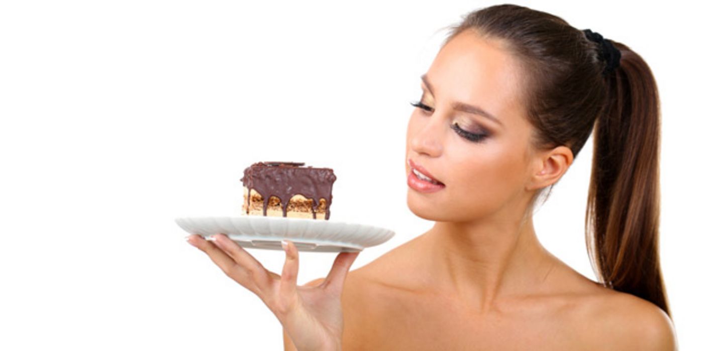 Junge Frau guckt prüfend auf ein Stück Kuchen auf einem Teller.