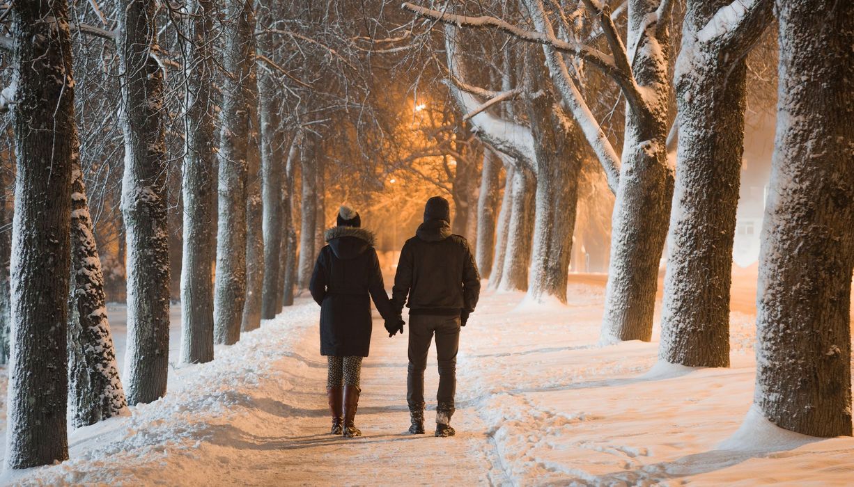 Händchen haltendes Paar macht einen Waldspaziergang im Winter.