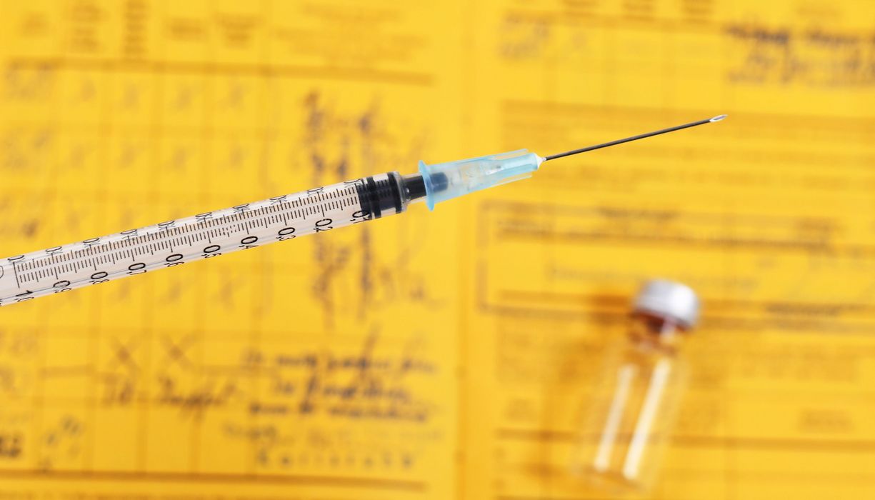Impfnadel vor einem gelben Impfpass.