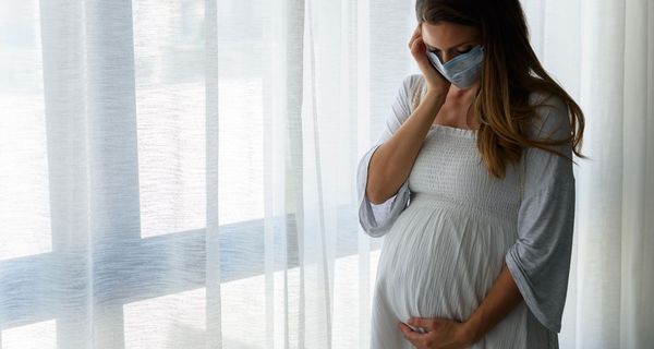 Schwangere Frau mit Maske, schaut auf ihren Bauch.