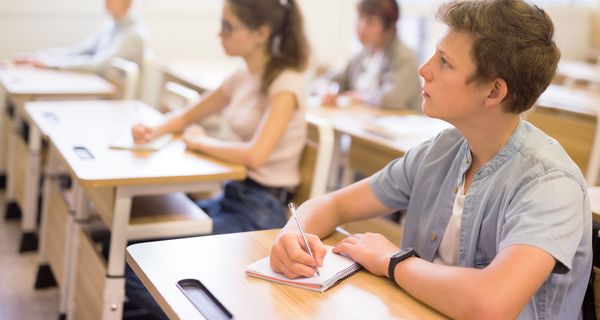 Junger Mann in der Schule, im Hintergrund Klassenkameraden an Schultischen.