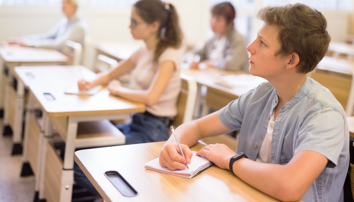 Junger Mann in der Schule, im Hintergrund Klassenkameraden an Schultischen.