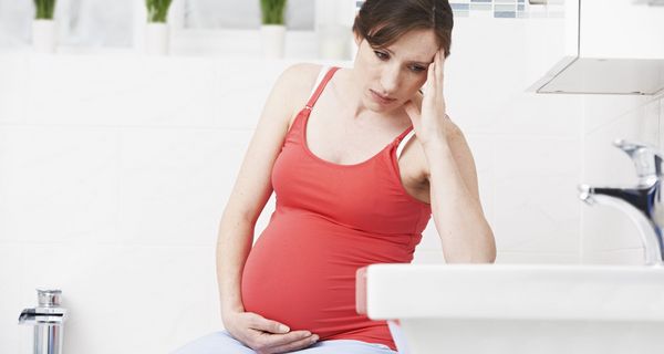 Schwangere Frau im Badezimmer, blickt konzentriert ins Waschbecken.
