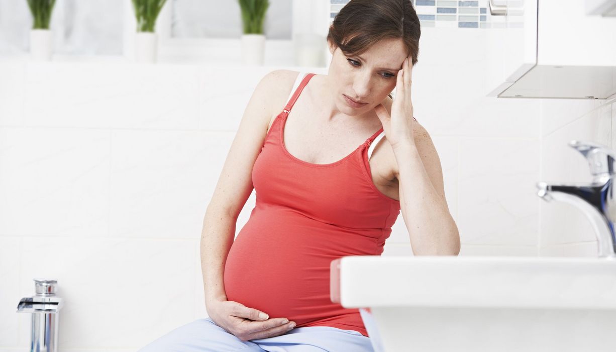 Schwangere Frau im Badezimmer, blickt konzentriert ins Waschbecken.